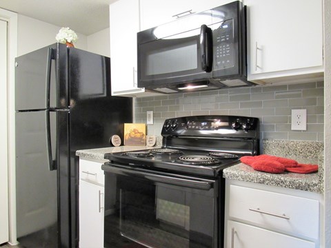 A black refrigerator and microwave in a kitchen with white cabinets.