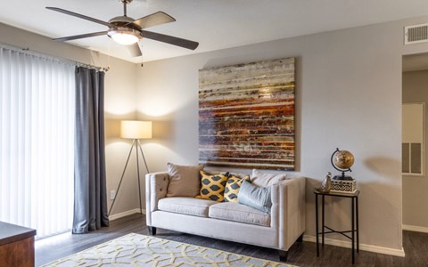 A living room with a couch, a ceiling fan, and a painting on the wall.