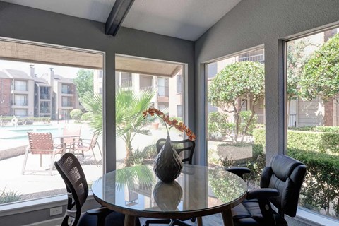 A dining table with chairs in front of a window with a view of a pool and buildings outside.