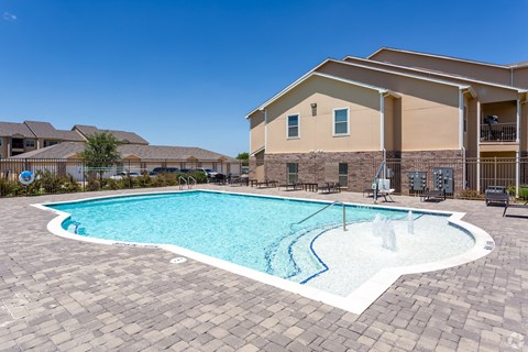 A swimming pool surrounded by a brick patio and a building in the background.