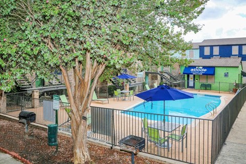 A pool surrounded by a fence with a blue umbrella and chairs.