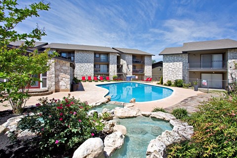 A swimming pool surrounded by rocks and plants in front of a building.