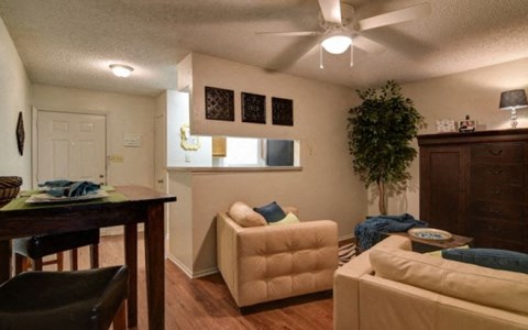 A living room with a beige couch, a dining table, and a ceiling fan.