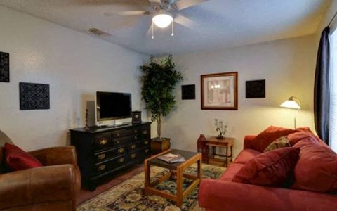 A living room with a brown leather chair, a red couch, a wooden coffee table, a television, and a ceiling fan.