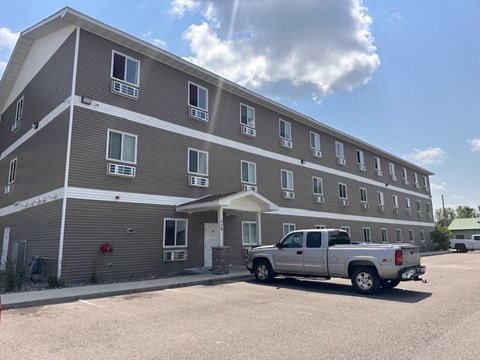 A silver truck is parked in front of a grey apartment building.