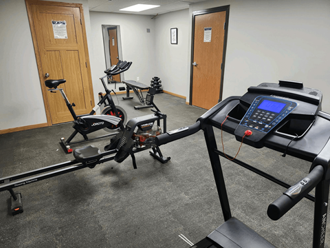 A gym room with a treadmill, elliptical trainer and a rowing machine.