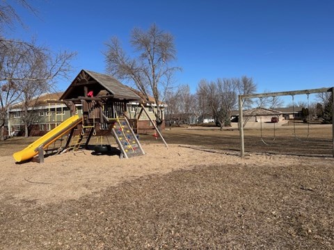 A playground with a yellow slide and a wooden structure.