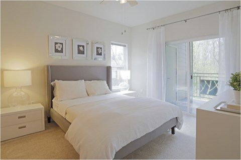 A bedroom with a large bed, a nightstand with a lamp, and a ceiling fan.
