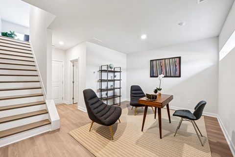 A living room with a staircase on the left and a dining table with chairs in the center.