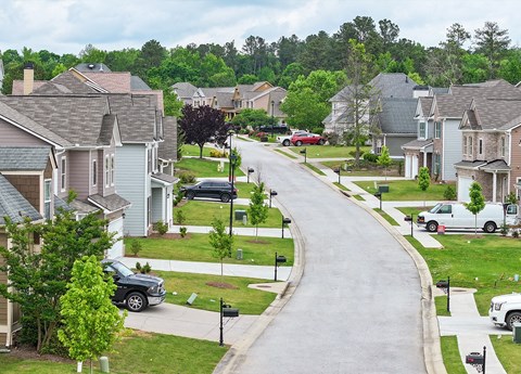 A residential street with houses on both sides and cars parked on the street.