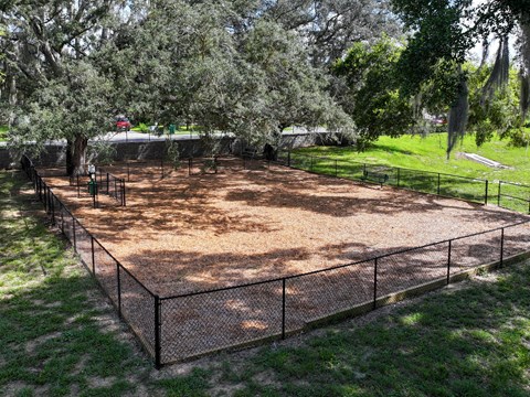 A fenced in area with a dirt ground and trees in the background.