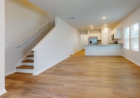 A spacious room with wooden floors and a staircase leading to the upper level.