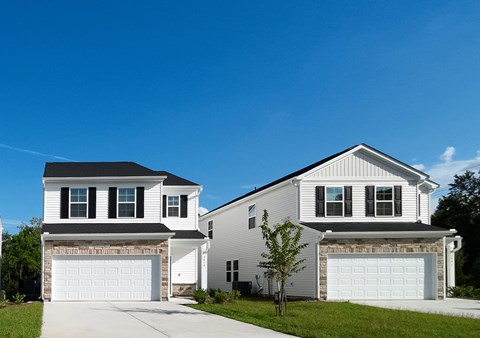 Two houses with garages are situated in a sunny suburban area.