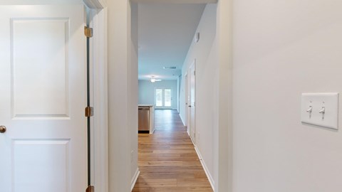 A hallway with a white door and a light switch on the wall.