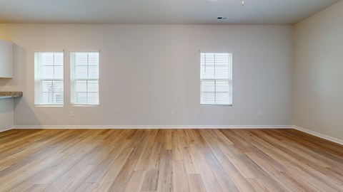 A room with wooden flooring and two windows.