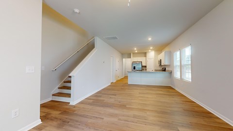 A spacious room with wooden floors and a staircase leading to the upper level.