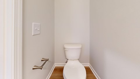 A white toilet in a small bathroom with a wooden floor.