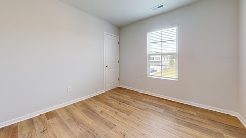 A room with wooden flooring and a window showing a building outside.