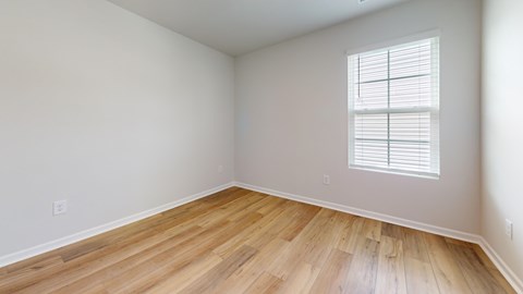 A room with wooden flooring and a window with blinds.