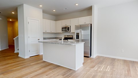 A kitchen with white cabinets and a white island with a refrigerator and microwave.