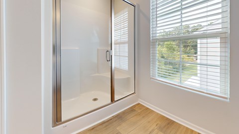 A white bathroom with a glass shower door and a window with blinds.