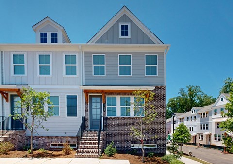 A modern two-story house with a grey and white exterior and a brick wall.