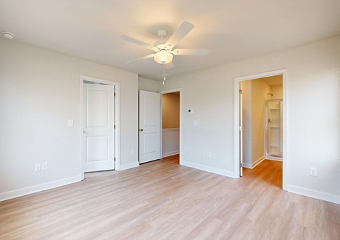 A room with a ceiling fan and light, hardwood floors, and white walls with two doors.