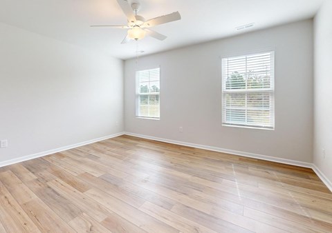 A room with a ceiling fan and two windows with blinds.