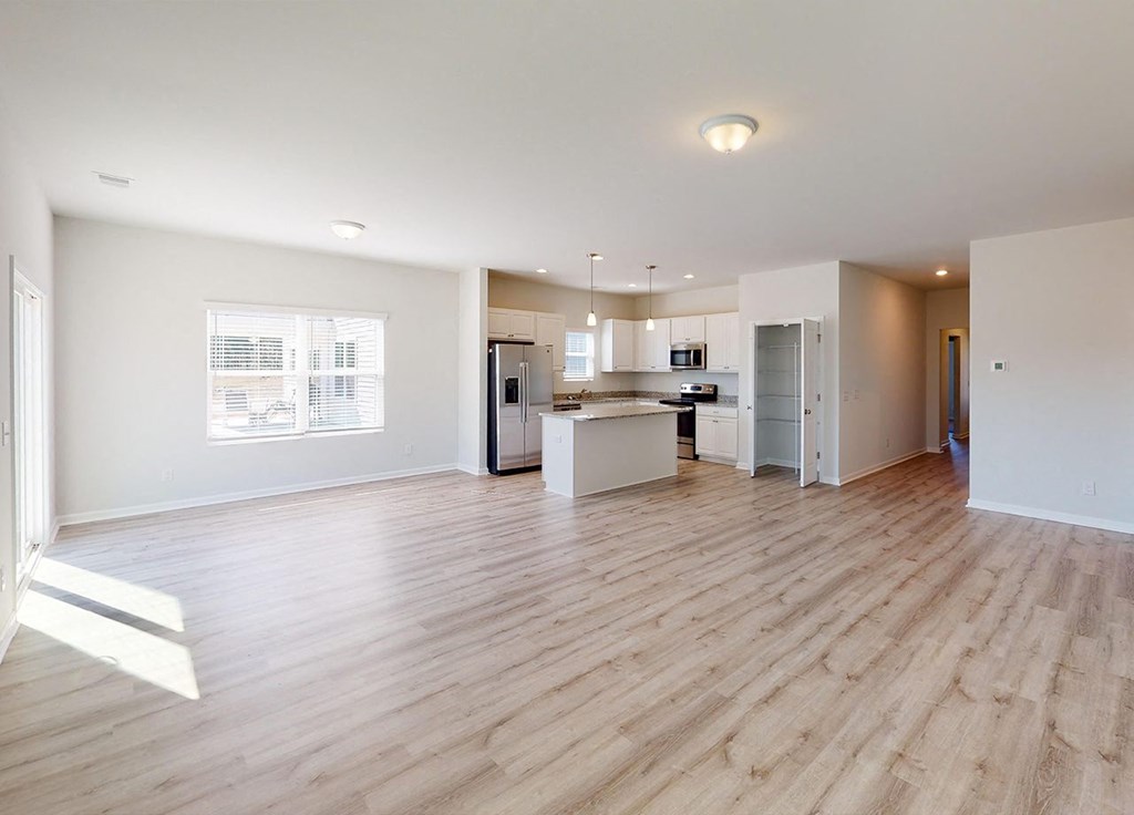 A spacious room with wooden flooring and a kitchen area in the background.