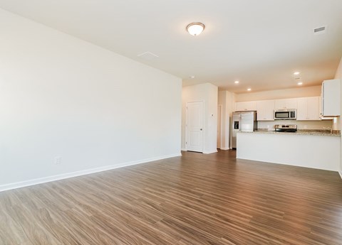A spacious room with wooden flooring and a kitchen area in the background.