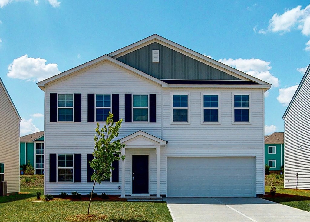 A white house with a black roof and a tree in front.