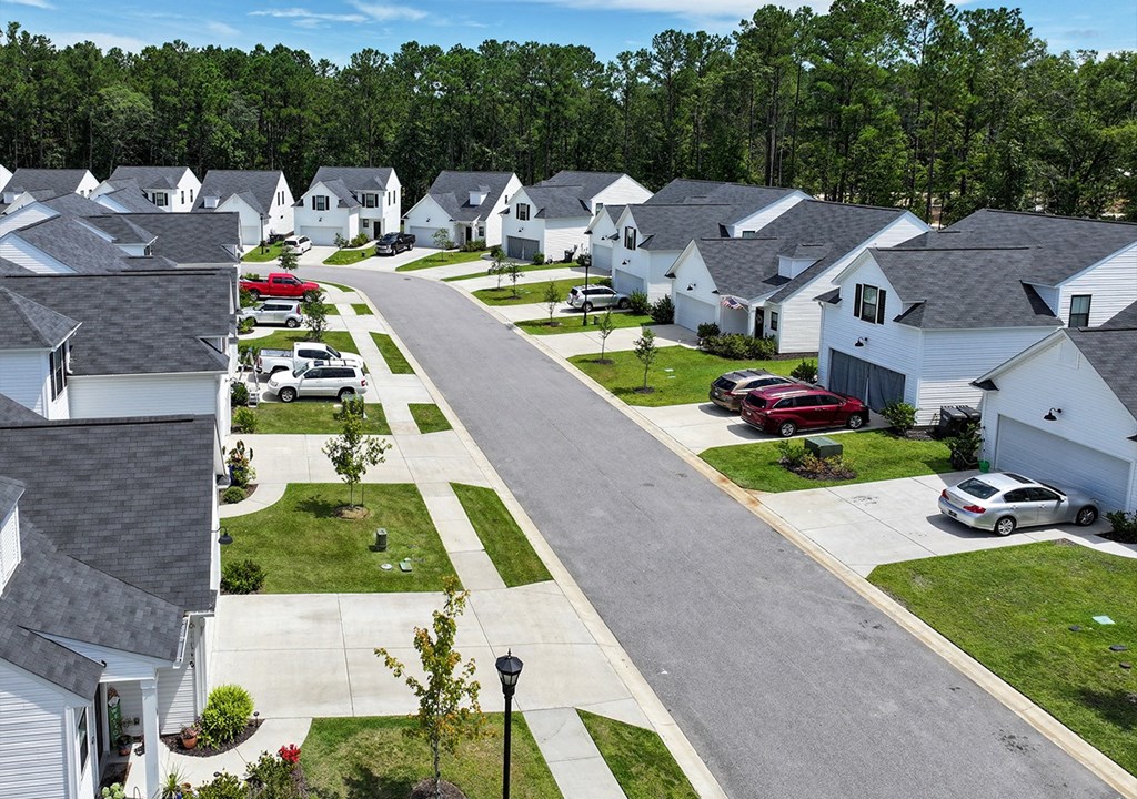 A residential street with houses on both sides and cars parked on the side.