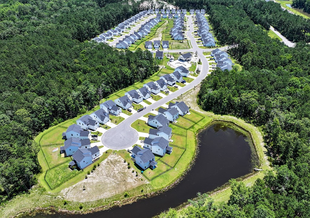 A bird's eye view of a residential area with houses surrounding a pond.