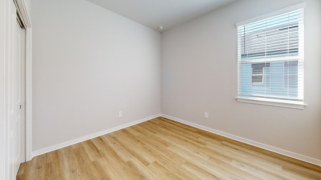 A room with wooden flooring and a window with blinds.