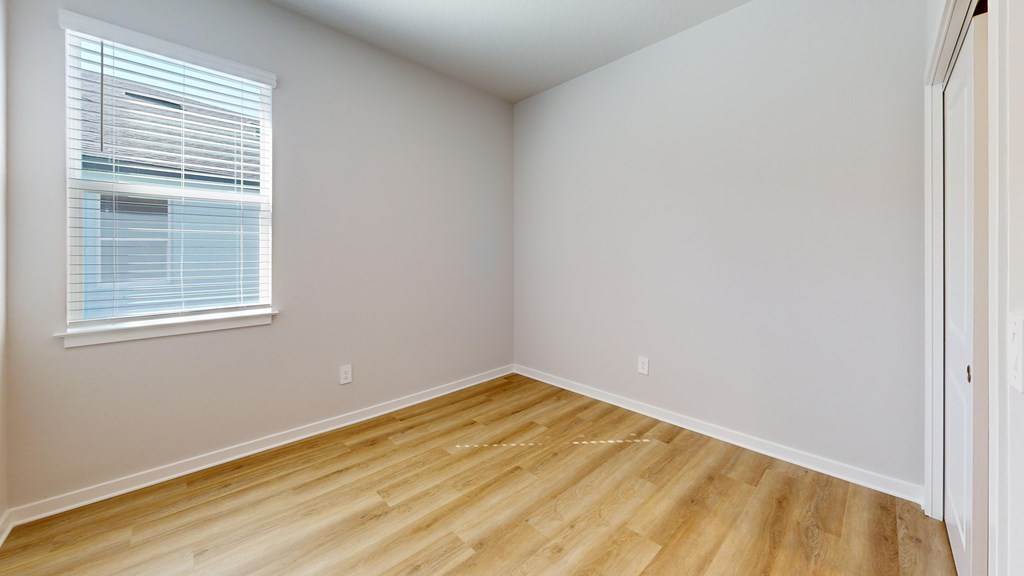 A room with wooden flooring and a window with blinds.