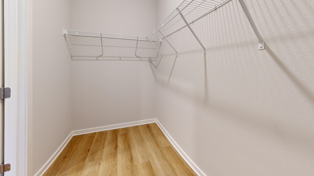 Empty white closet with wooden floor and shelves.