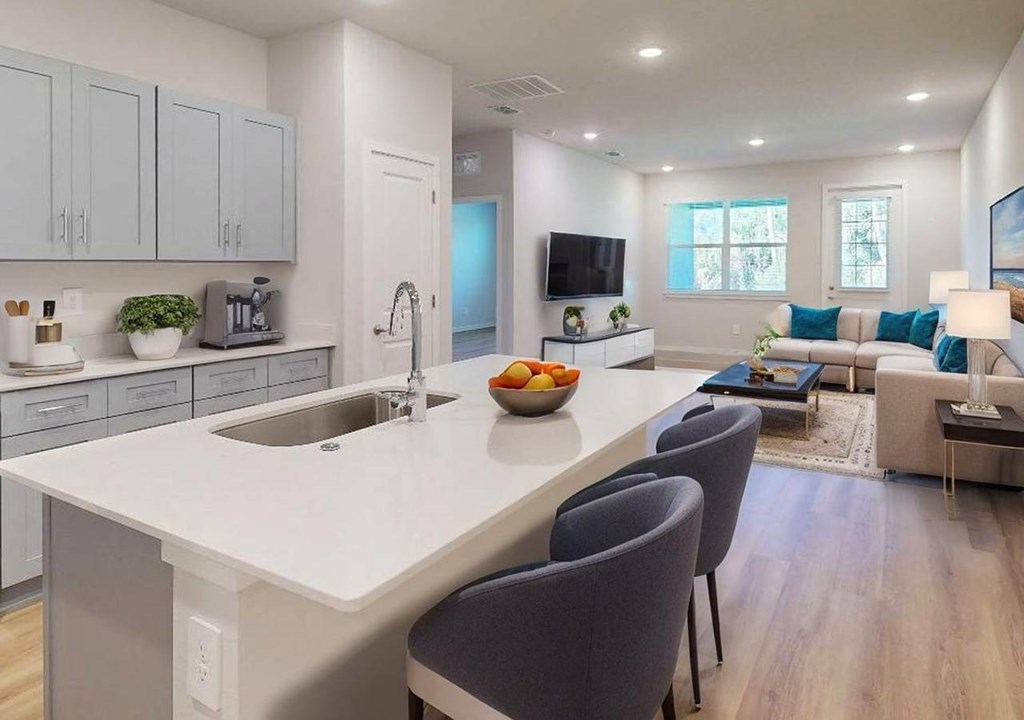 A modern kitchen with a white countertop and grey chairs.
