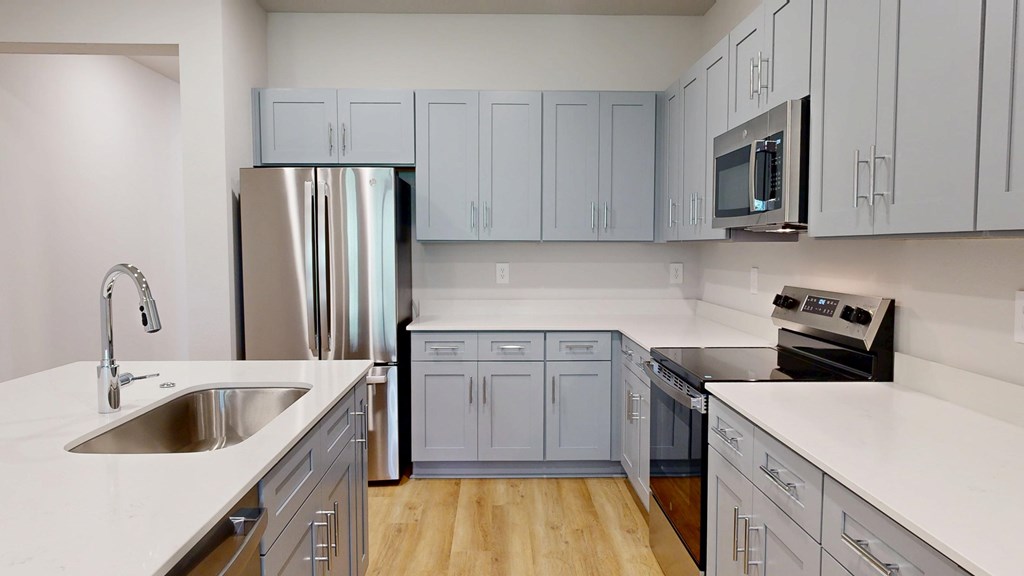 A kitchen with a stainless steel refrigerator, a white countertop, and a wooden floor.