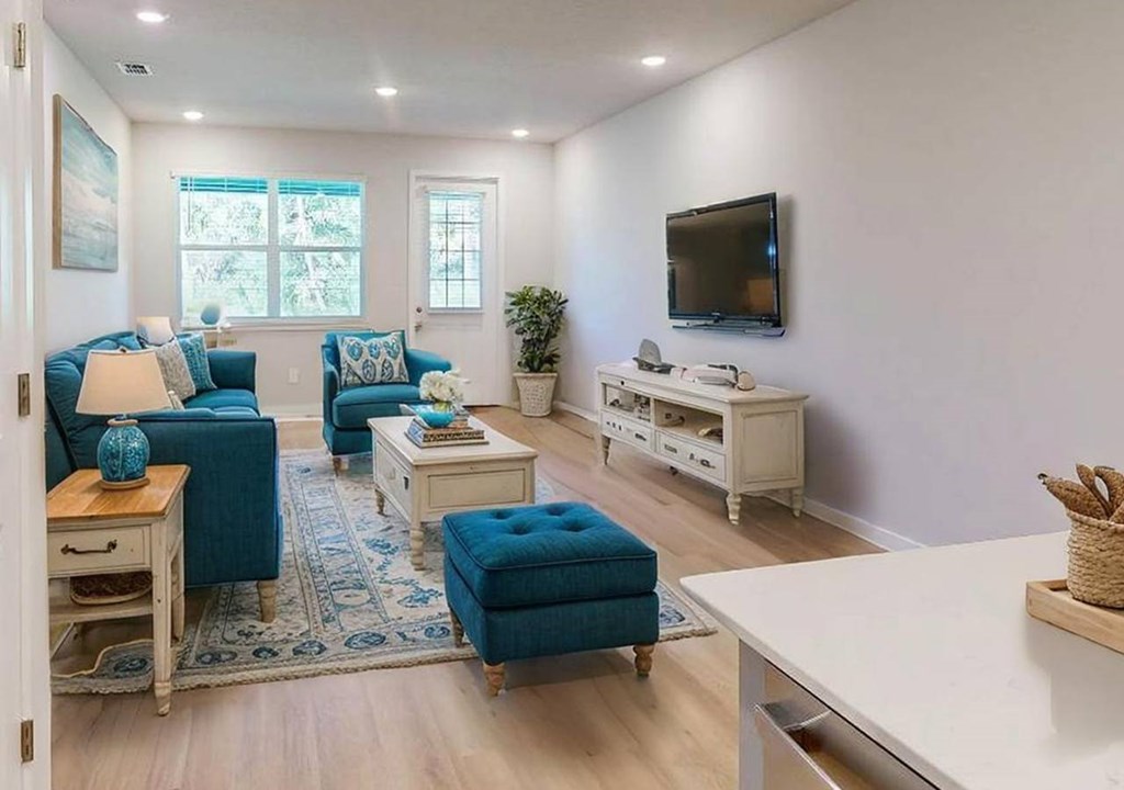 A living room with a blue couch, a white coffee table, and a flat screen TV mounted on the wall.