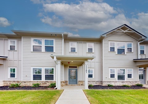 A two-story residential building with a front yard and a clear sky.