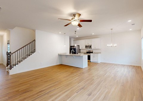A spacious living room with a staircase and a kitchen area.