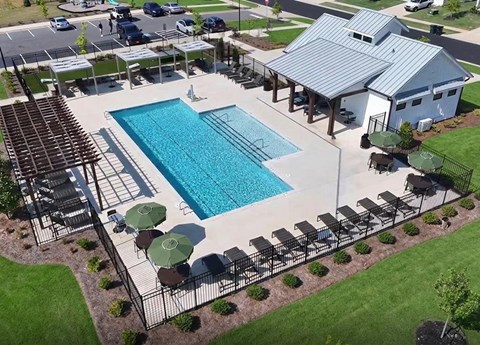 An outdoor pool area with a large rectangular pool, a pergola, and a small building.