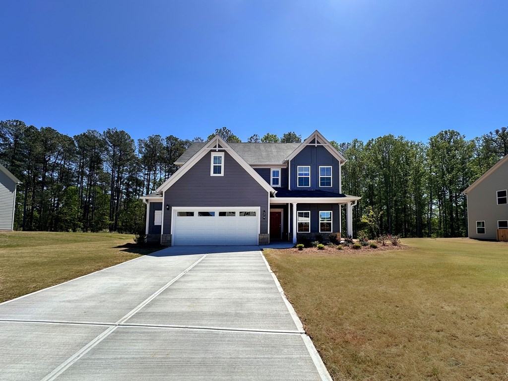 A two-story house with a garage is surrounded by a grassy area and trees.