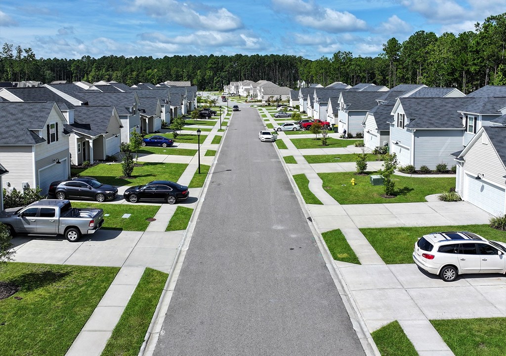 A residential street with houses on both sides and cars parked on the side.