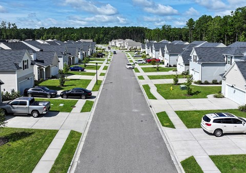 A residential street with houses on both sides and cars parked on the side.