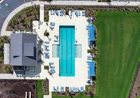 An aerial view of a pool surrounded by lawn chairs and a building.