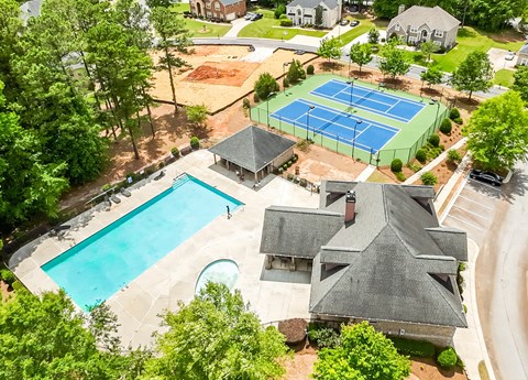 A tennis court is surrounded by a pool and a house.