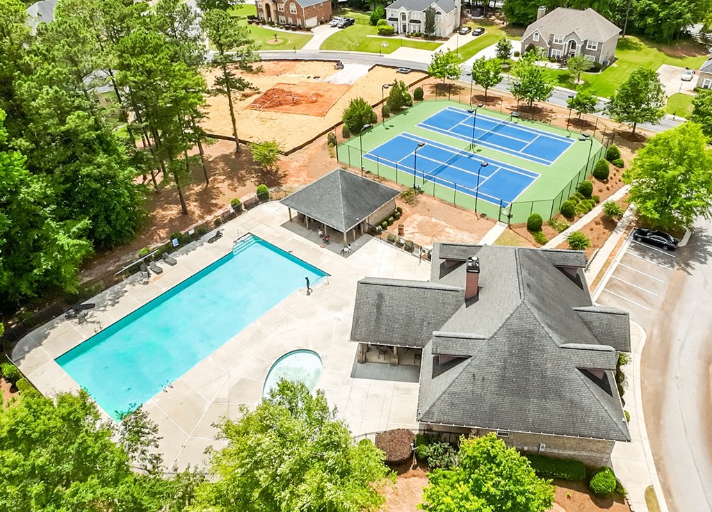 A tennis court is surrounded by a pool and a house.