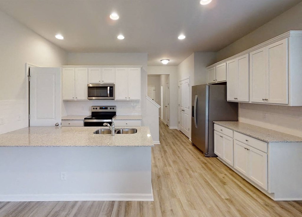 A modern kitchen with white cabinets and a wooden floor.