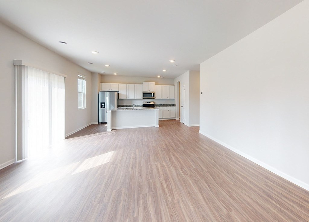 A spacious kitchen with wooden flooring and white walls.